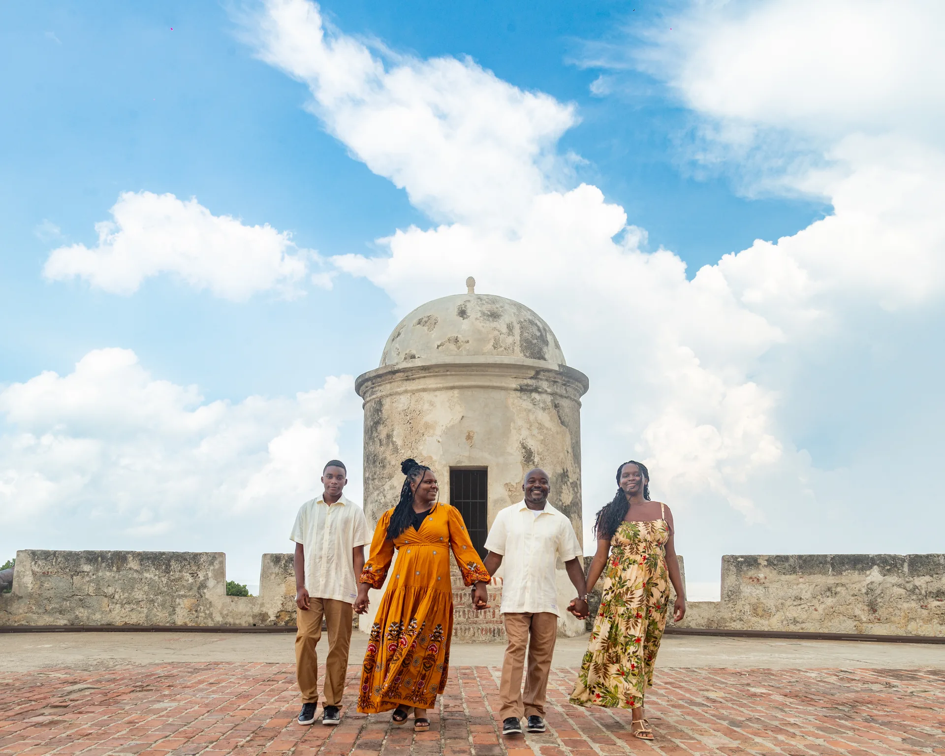 Familia de cuatro tomada de la mano sobre las murallas de Cartagena, frente a una garita colonial